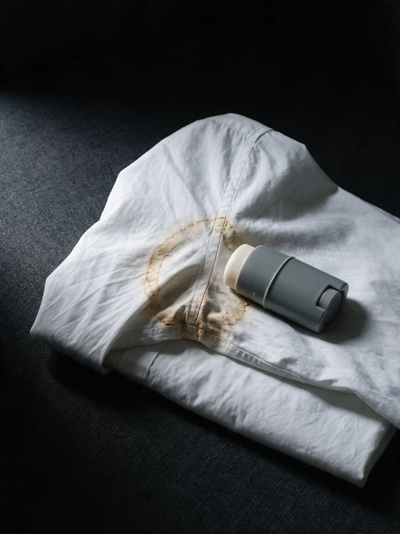 White shirt with a yellow underarm stain beside the old antiperspirant stick that caused it