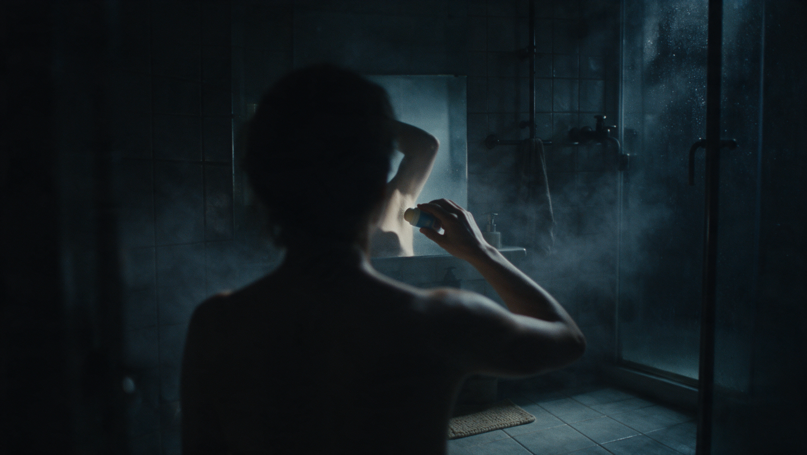 Someone applying deodorant at a mirror in a dark bathroom